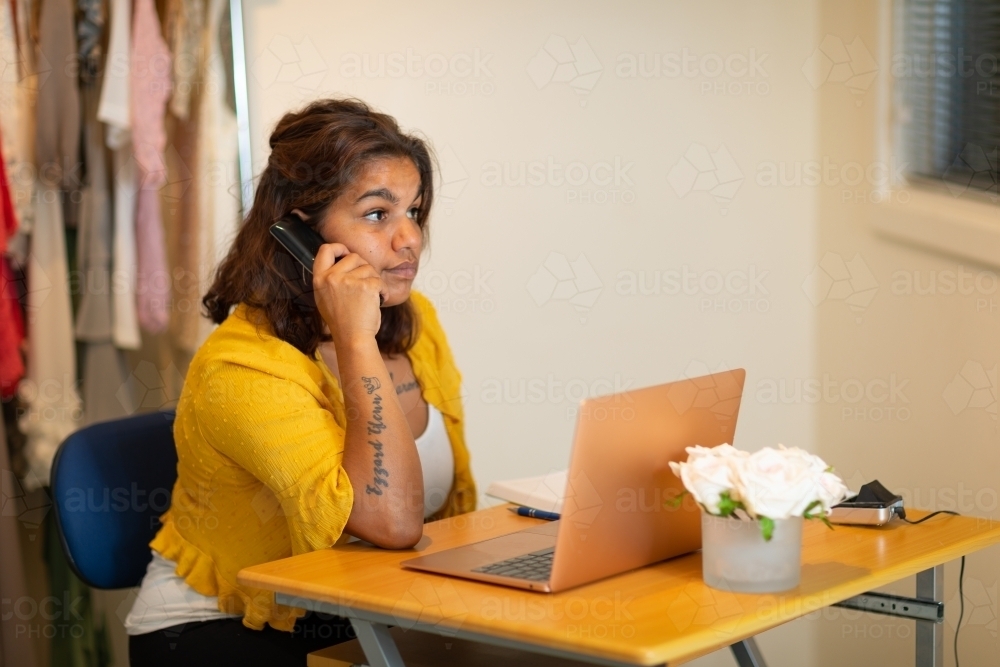 aboriginal woman sitting at desk with laptop computer and telephone - Australian Stock Image