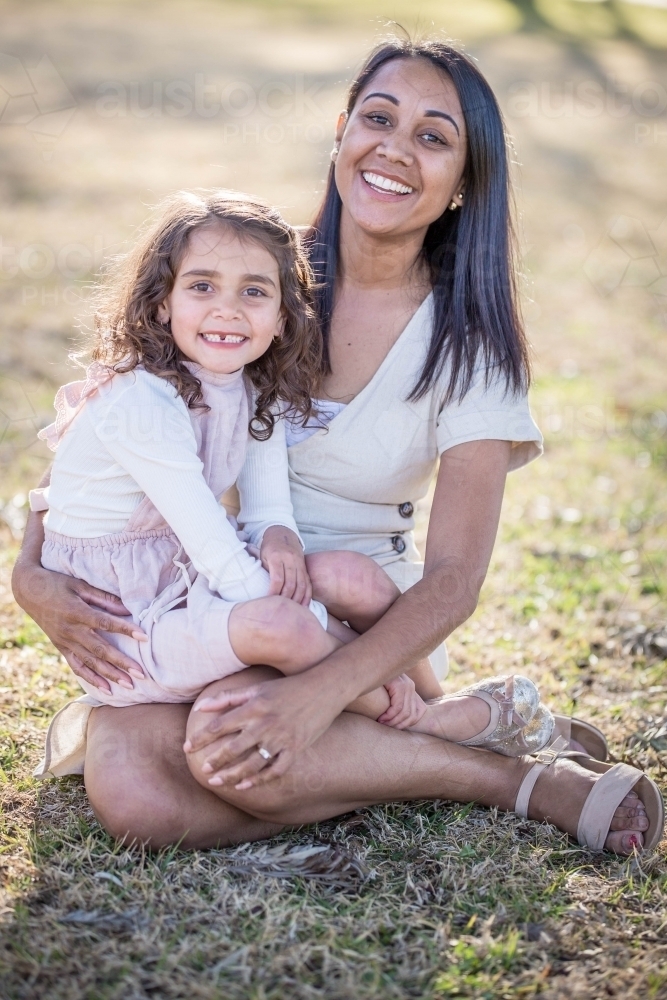 Aboriginal woman sitting with mixed race child on lap smiling - Australian Stock Image
