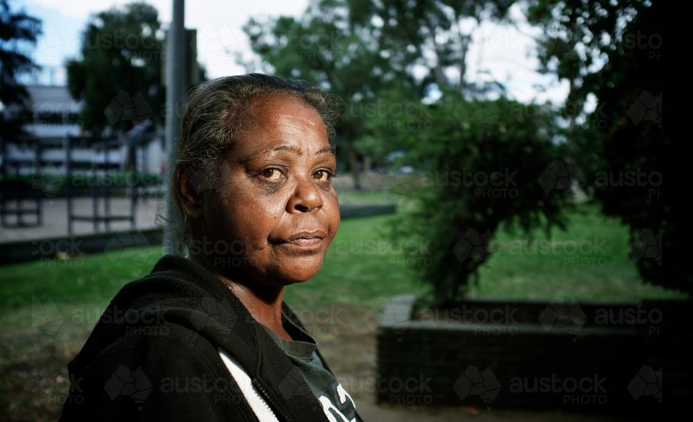 Aboriginal Woman wearing black hoodie sitting outdoors - Australian Stock Image
