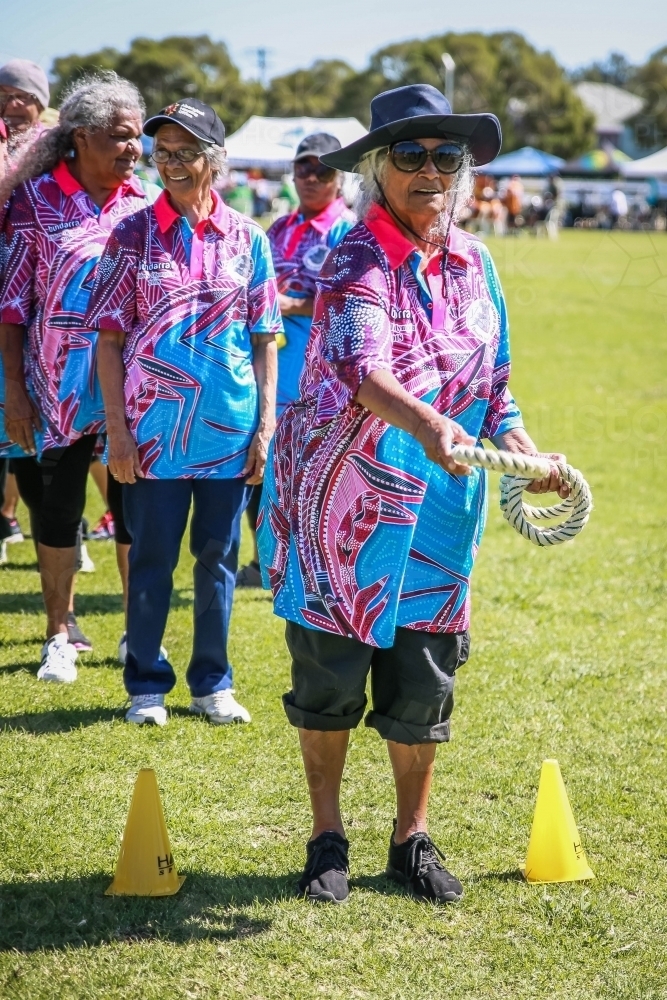 Aboriginal woman wearing hat and glasses throwing rope ring quoits - Australian Stock Image