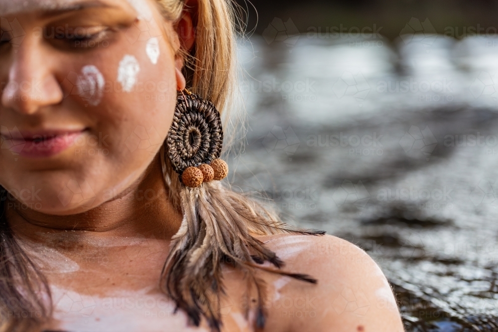 aboriginal woman with woven earring and ochre paint on face focus on earing - Australian Stock Image