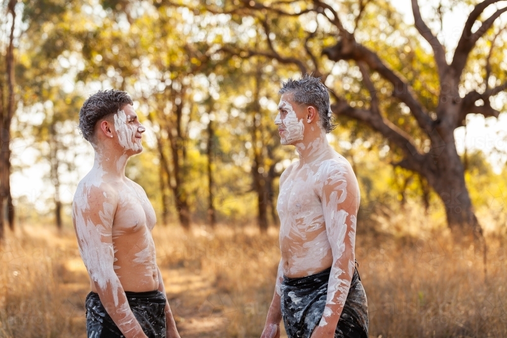 Aboriginal young men in body paint talking together in bush - Australian Stock Image