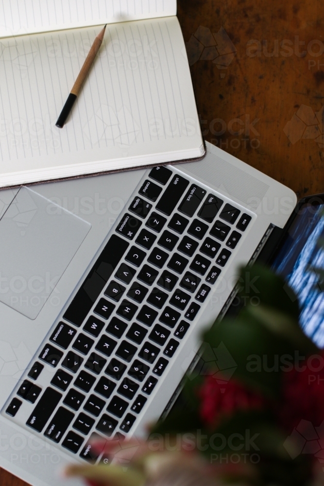 Above angle close up shot of laptop keyboard with open notebook - Australian Stock Image