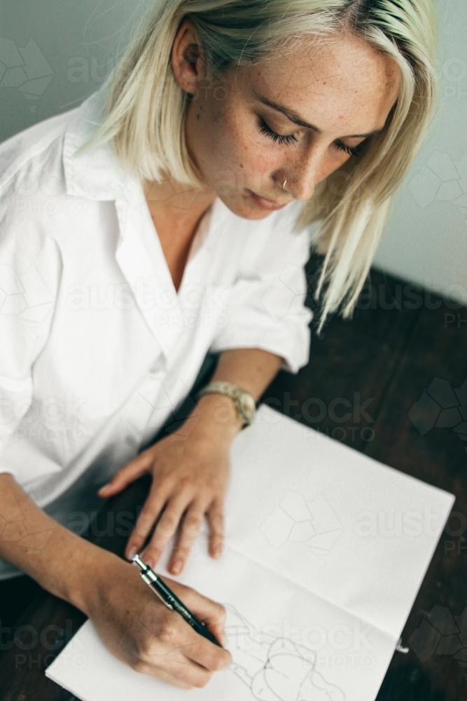 Above angled shot of young blonde woman drawing in a sketch book - Australian Stock Image