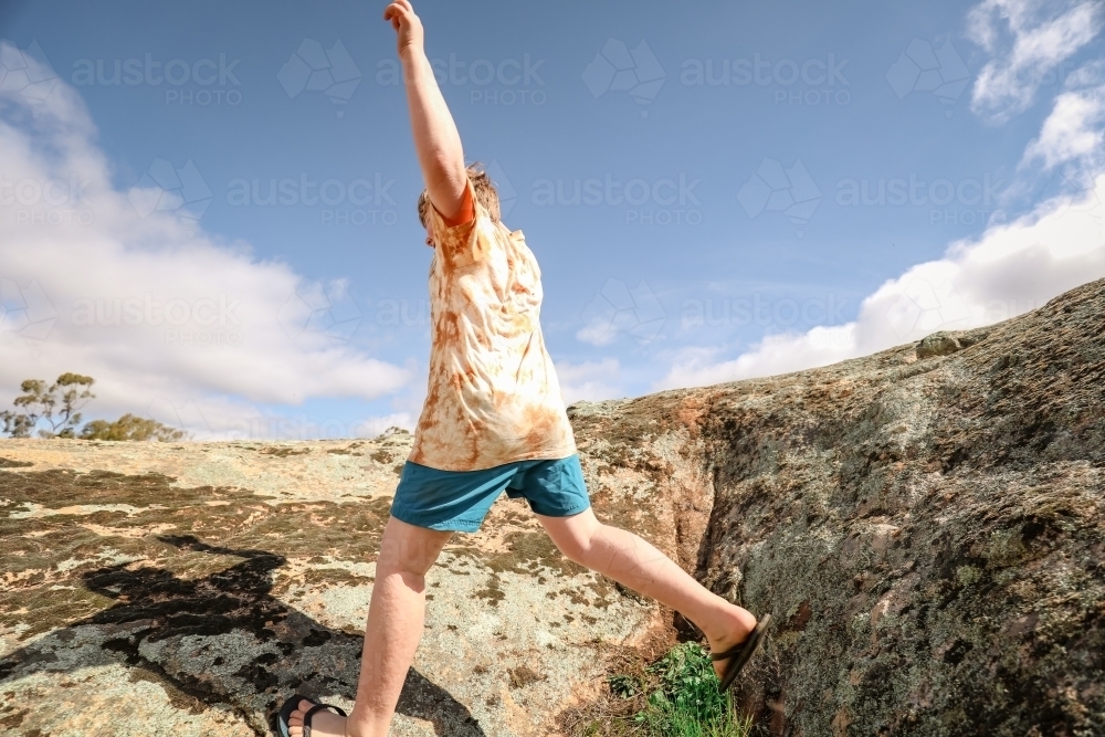 Active child running and jumping over rocks under blue sky - Australian Stock Image