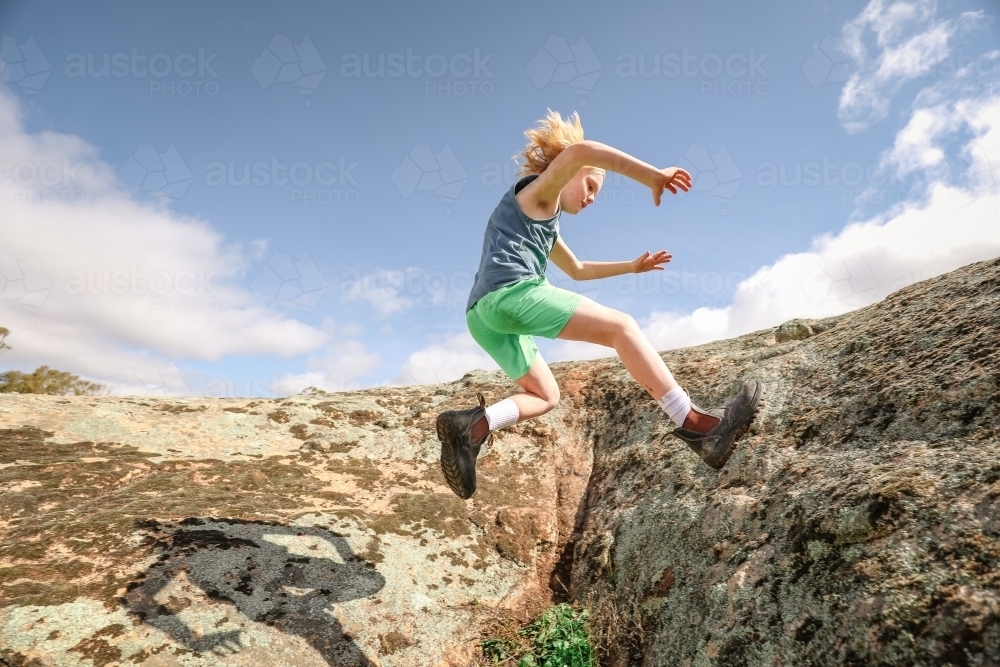 Active child running and jumping over rocks under blue sky - Australian Stock Image