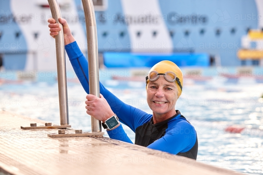 Active senior lady climbing into in swimming pool - Australian Stock Image