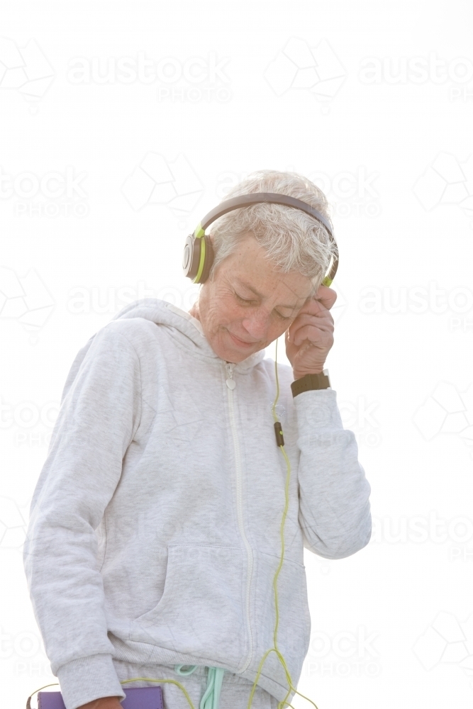 Active senior lady listening to music with headphones - Australian Stock Image