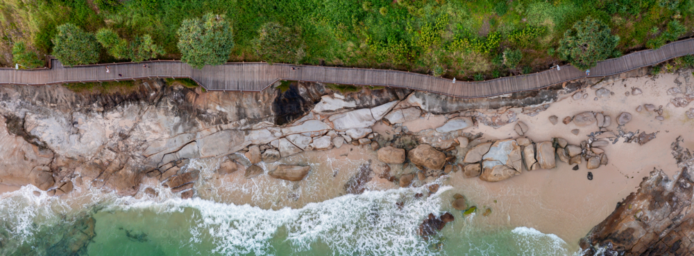 Aerial panorama of a coastal boardwalk above a rocky beach and breaking waves - Australian Stock Image