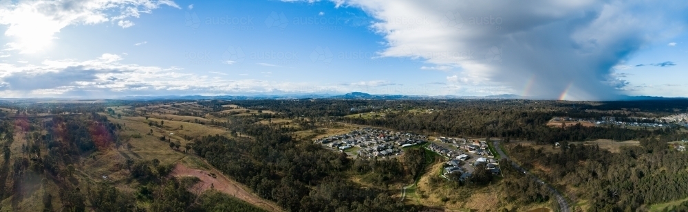 Aerial panorama of double rainbows and rain cloud over edge of residential area - Australian Stock Image