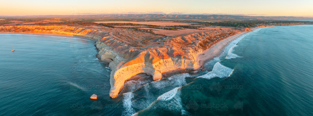 Aerial panorama of dramatic eroded cliffs along a rugged coastline at sunset - Australian Stock Image