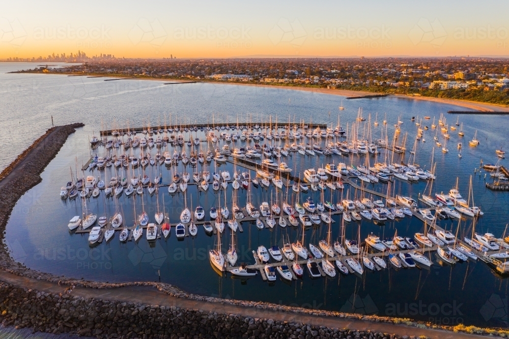 Aerial view of a bay side marina with rows of boats tied to jetties behind a large rock breakwater - Australian Stock Image