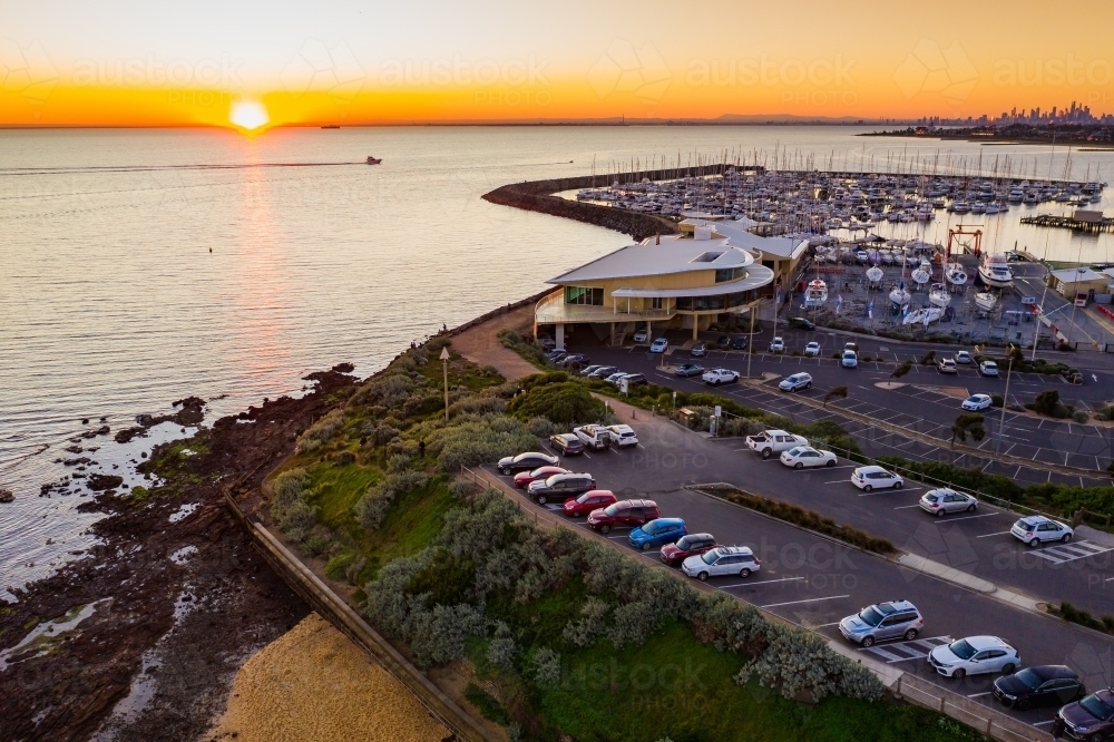 Aerial view of a bay side yacht club and car park above a beach at sunset - Australian Stock Image