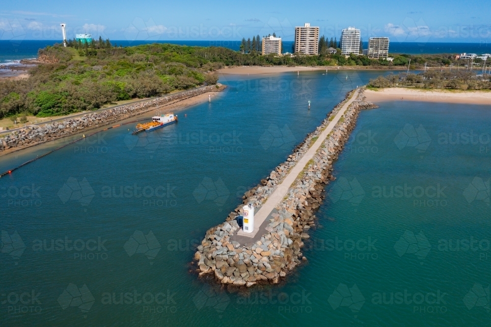 Aerial view of a beacon at the end of a rocky breakwaters with apartment buildings in the distance - Australian Stock Image