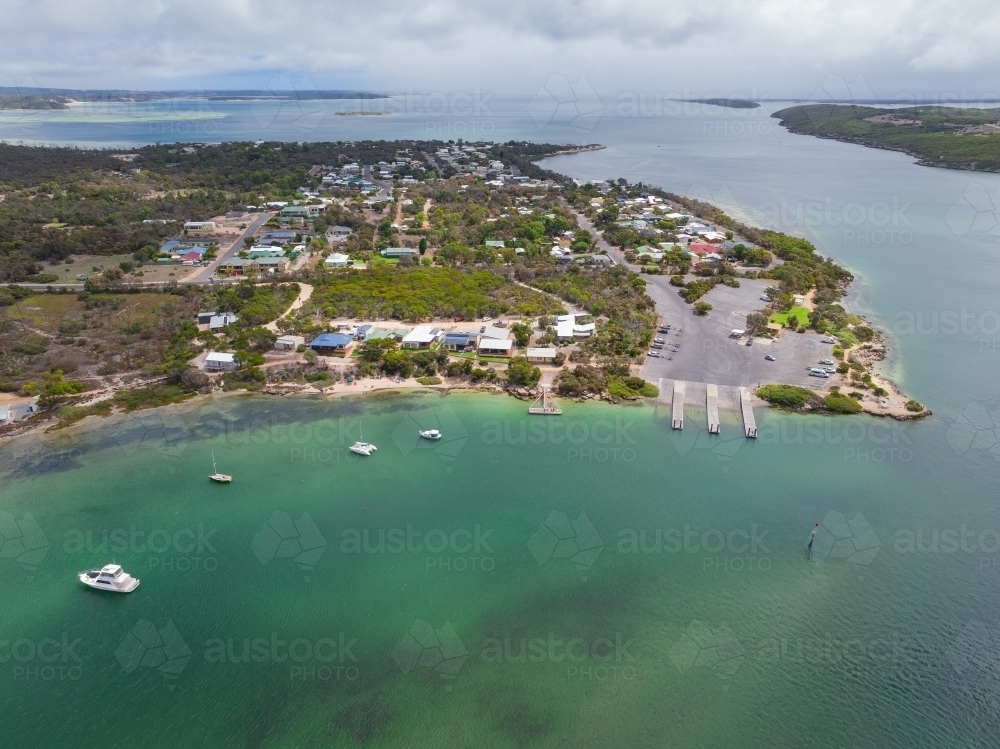 Aerial view of a boat ramp at a small coastal town alongside a calm ocean bay - Australian Stock Image