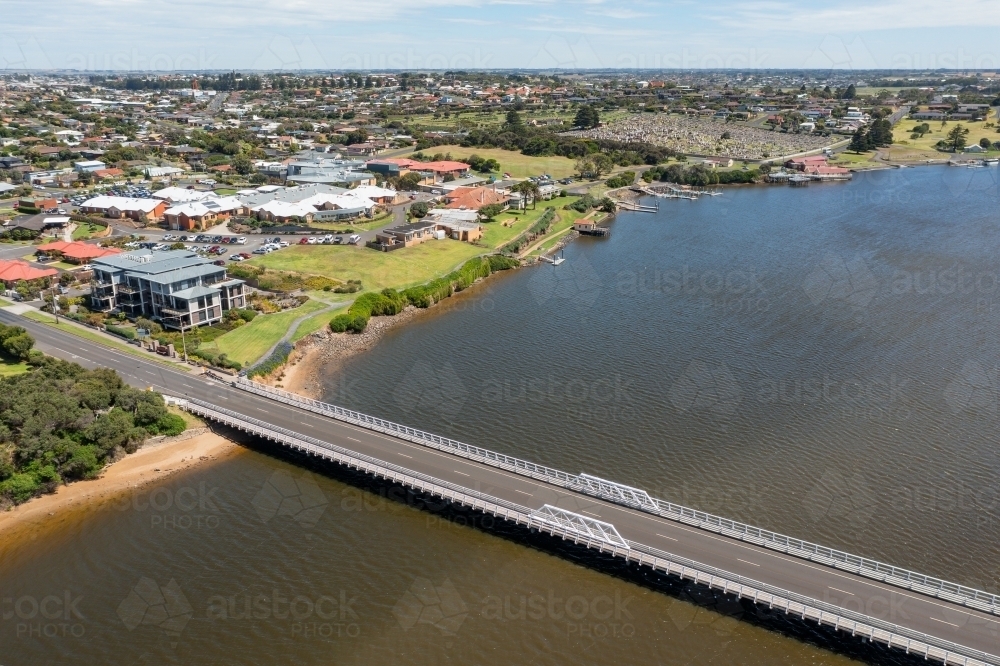 Aerial view of a bridge over a wide brown river with a town on the riverbank - Australian Stock Image