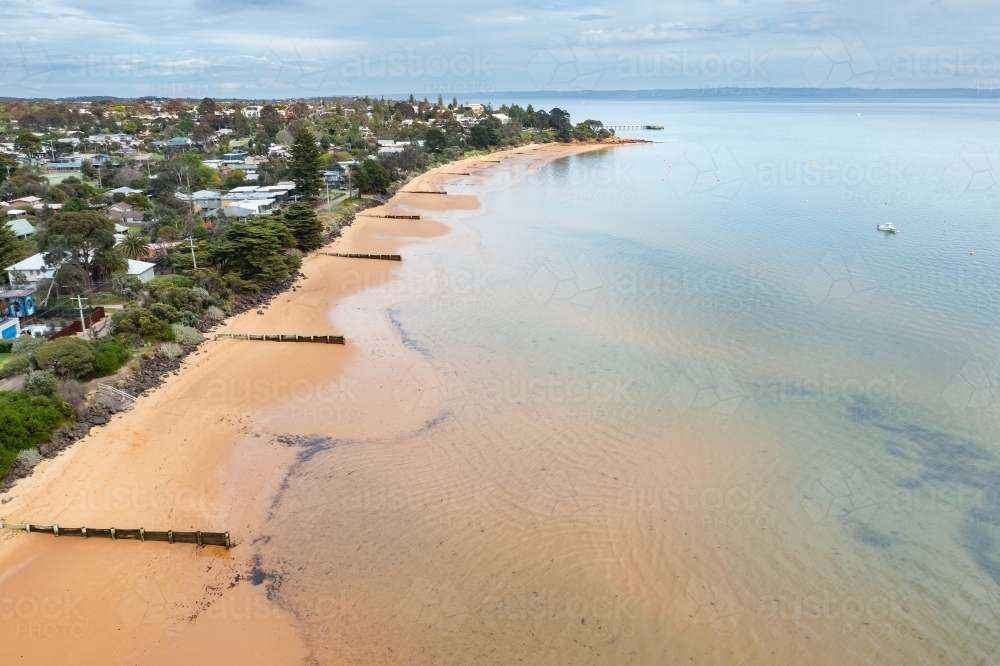 Aerial view of a calm bay and golden sandy beach with lines of groynes - Australian Stock Image