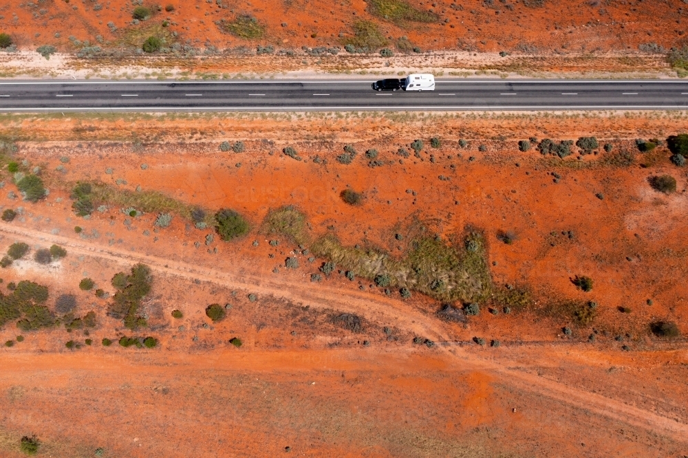 Aerial view of a car towing a caravan along a straight road through a barren red outback landscape - Australian Stock Image