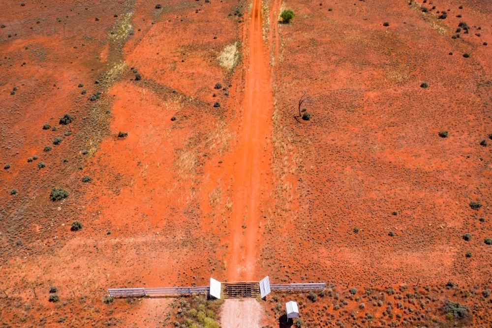 Aerial view of a cattle grate in a dirt track across red barren land - Australian Stock Image