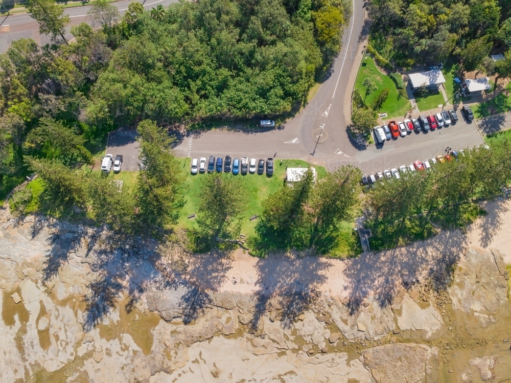 Aerial view of a coastal car park above a beach with a row of pine trees - Australian Stock Image