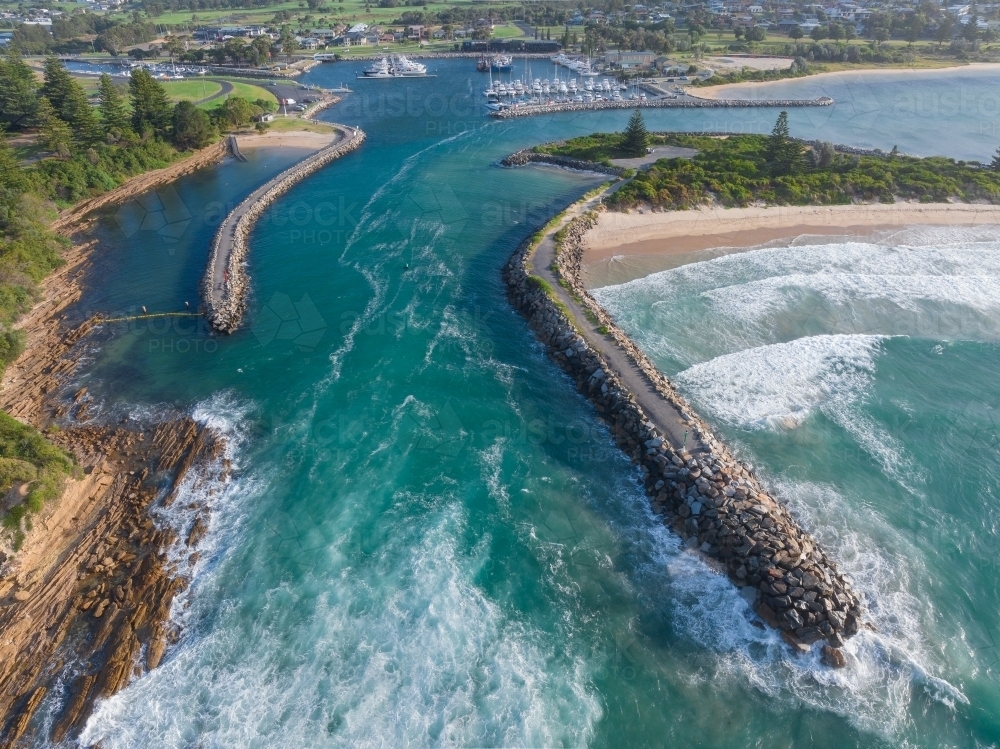 Aerial view of a coastal river flowing out to sea between rock breakwaters - Australian Stock Image