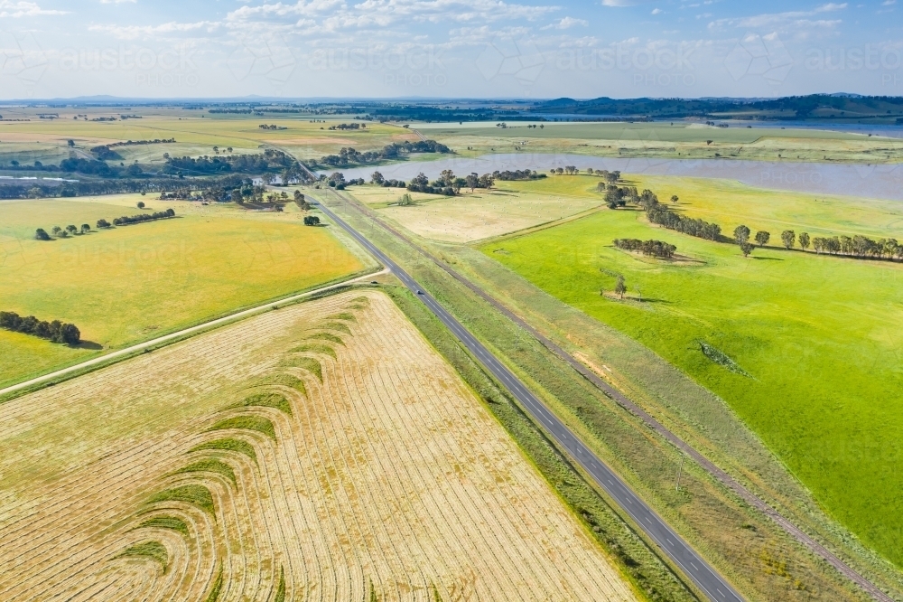 Aerial view of a country road running between paddocks and over lake - Australian Stock Image