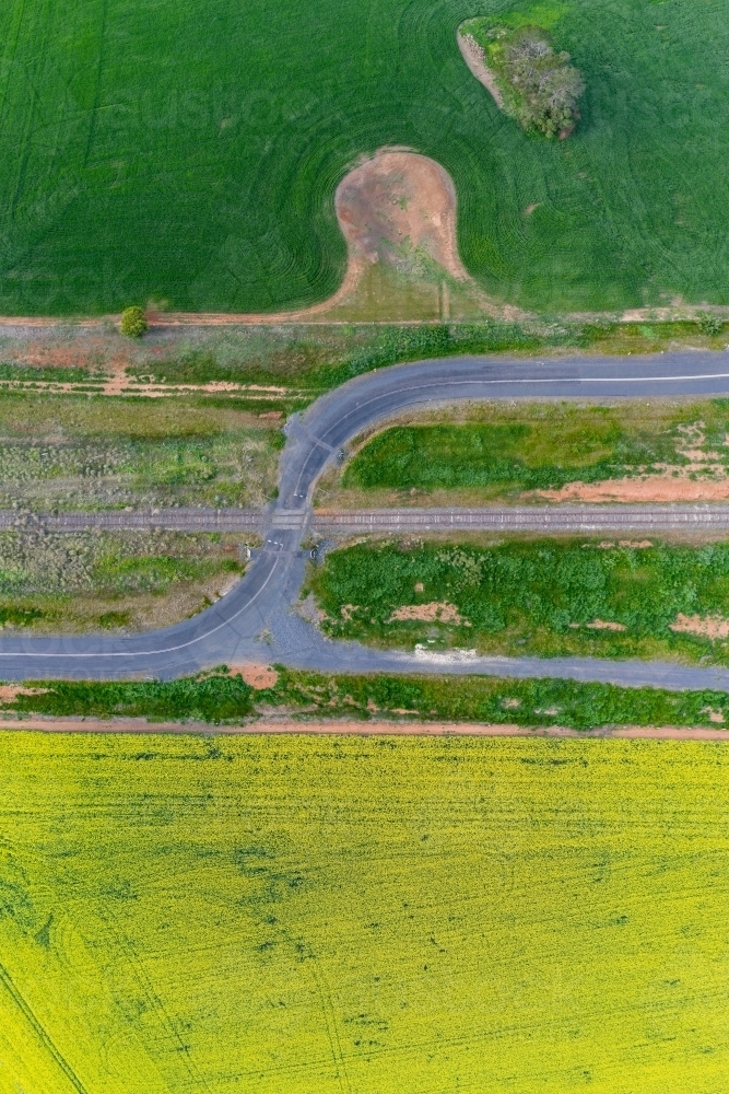 Aerial view of a country road winding through a railway crossing along side farmland - Australian Stock Image