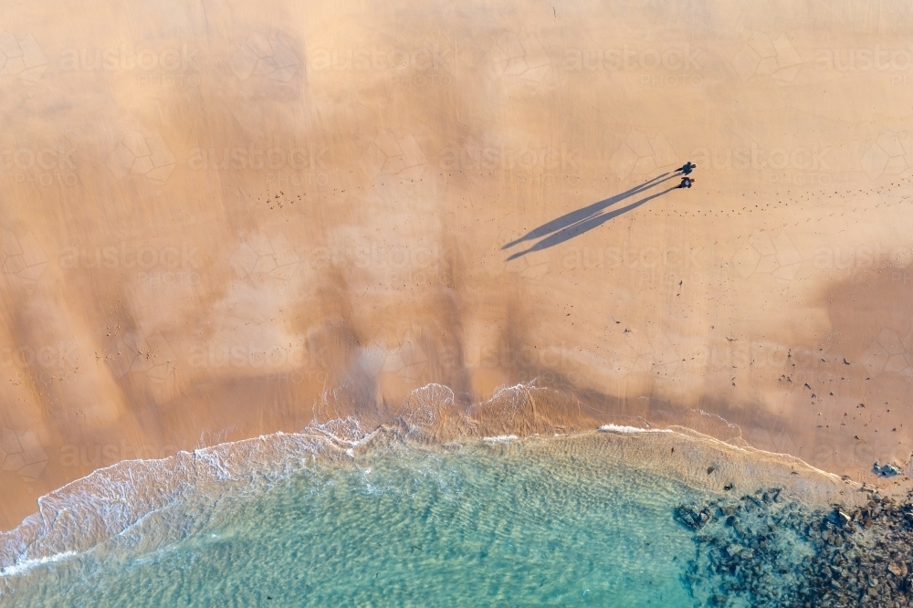 Aerial view of a couple walking on a wide sandy beach castling long shadows - Australian Stock Image