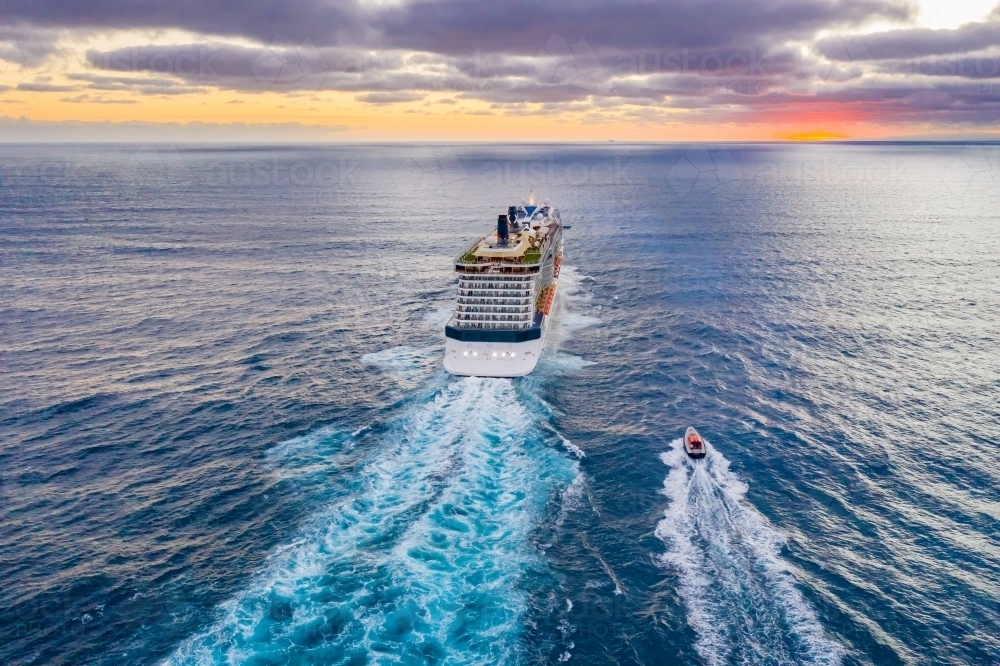 Aerial view of a cruise ship heading out to sea at sunset - Australian Stock Image