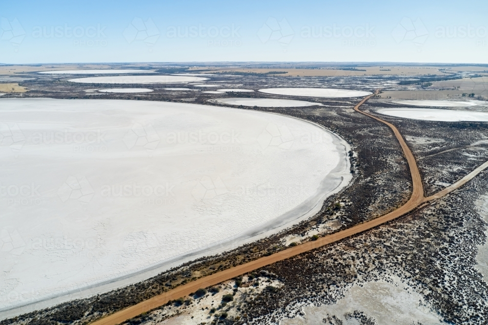 Aerial view of a dirt road and salt lakes covering the landscape in rural Western Australia. - Australian Stock Image