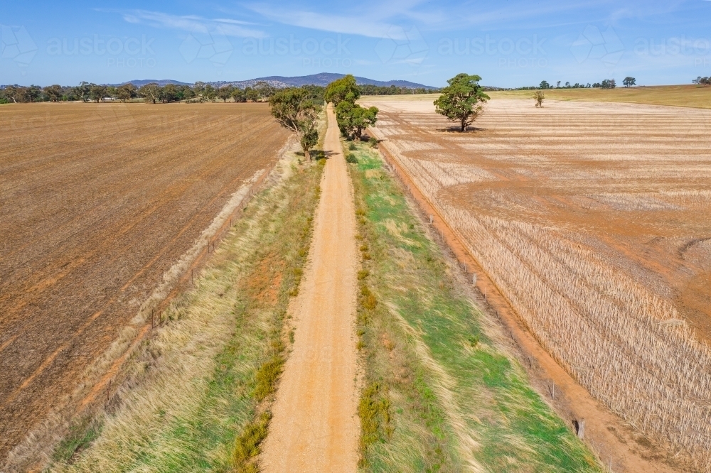 Aerial view of a dirt road between paddocks of drying stubble - Australian Stock Image