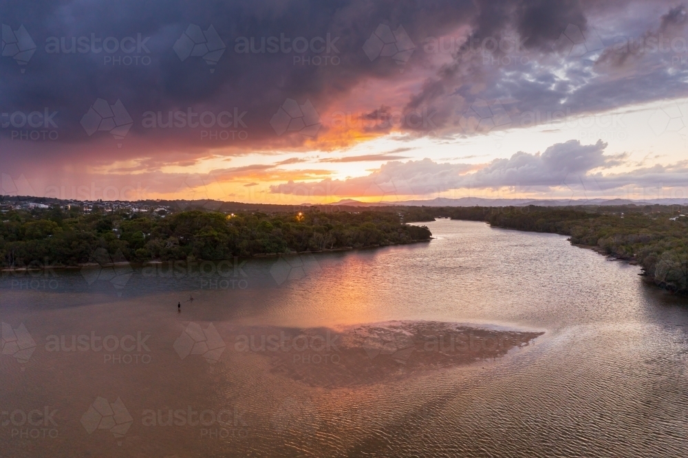 Aerial view of a dramatic sunset sky over an inland river flowing past coastal vegetation - Australian Stock Image