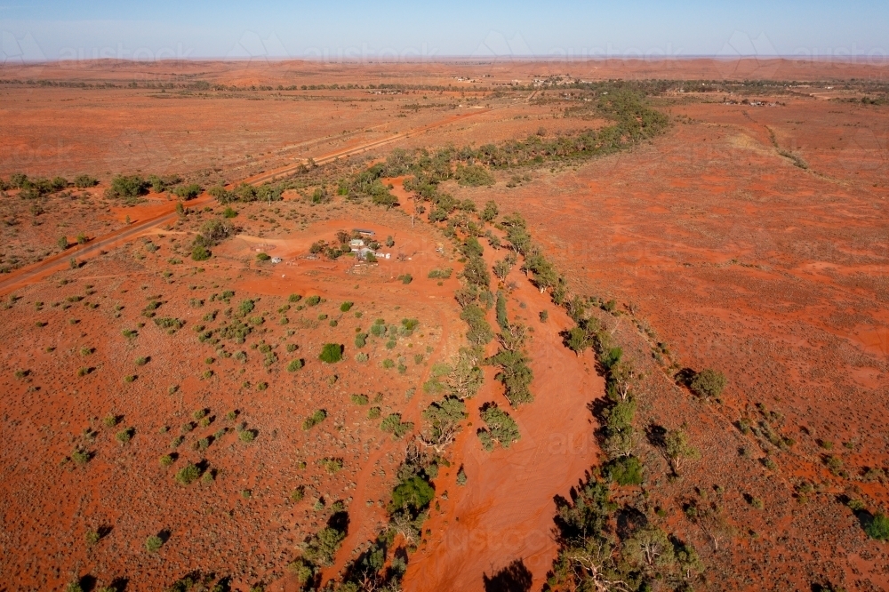 Aerial view of a dry red soil river bed lined with gum trees winding through an arid landscape - Australian Stock Image