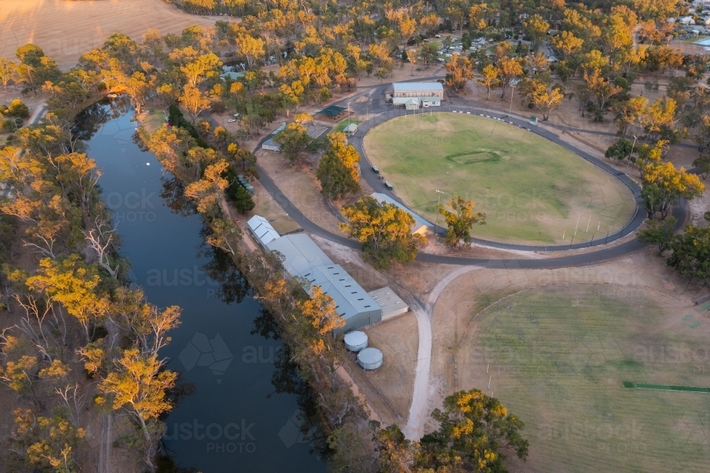Aerial view of a dry sports oval and buildings alongside a river surrounded by gum trees - Australian Stock Image