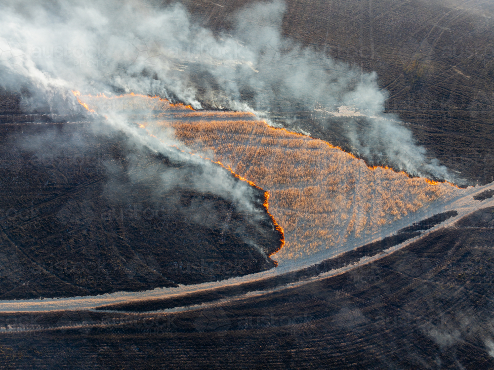 Aerial view of a fire burning off stubble in a blackened paddock - Australian Stock Image