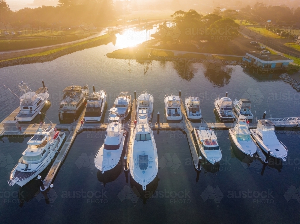 Aerial view of a foggy sunrise over boats moored along jetty in a coastal marina - Australian Stock Image