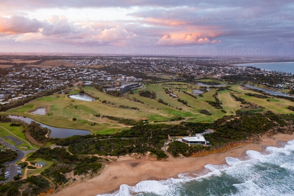 Aerial view of a golf course next to a sandy beach with coloured clouds overhead - Australian Stock Image