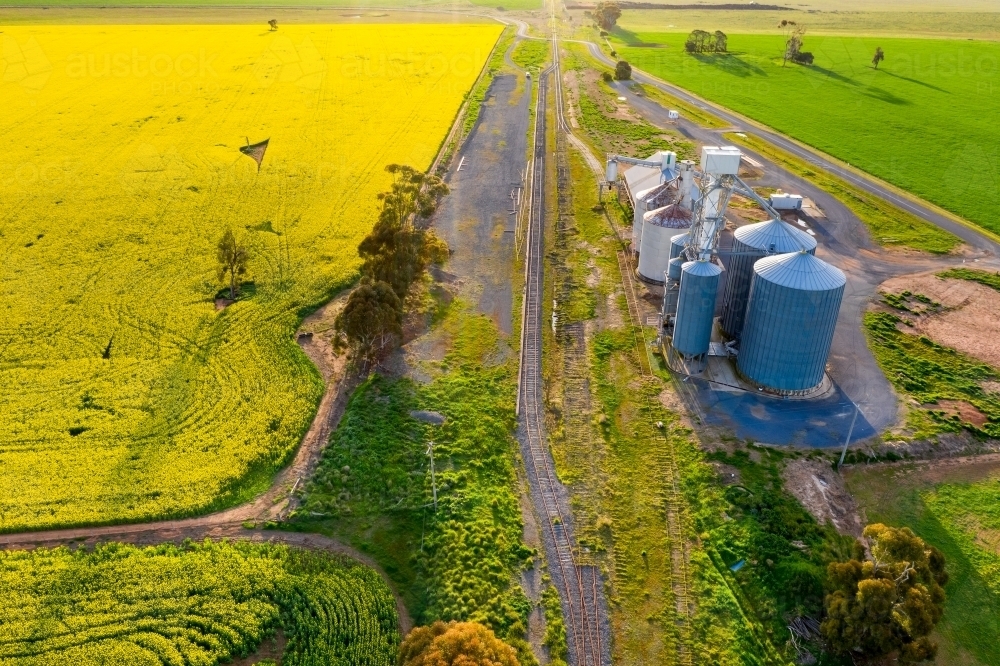 Aerial view of a grain  silo along side a railway line and a canola field - Australian Stock Image