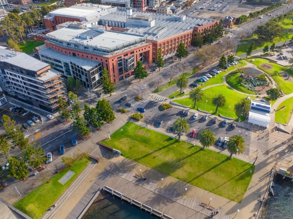 Aerial view of a green city waterfront reserve alongside an esplanade and high rise buildings - Australian Stock Image