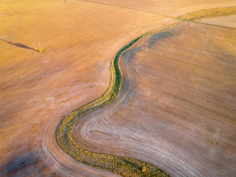 Aerial view of a green creek bed winding through a ploughed paddock at Dimboola in Victoria - Australian Stock Image