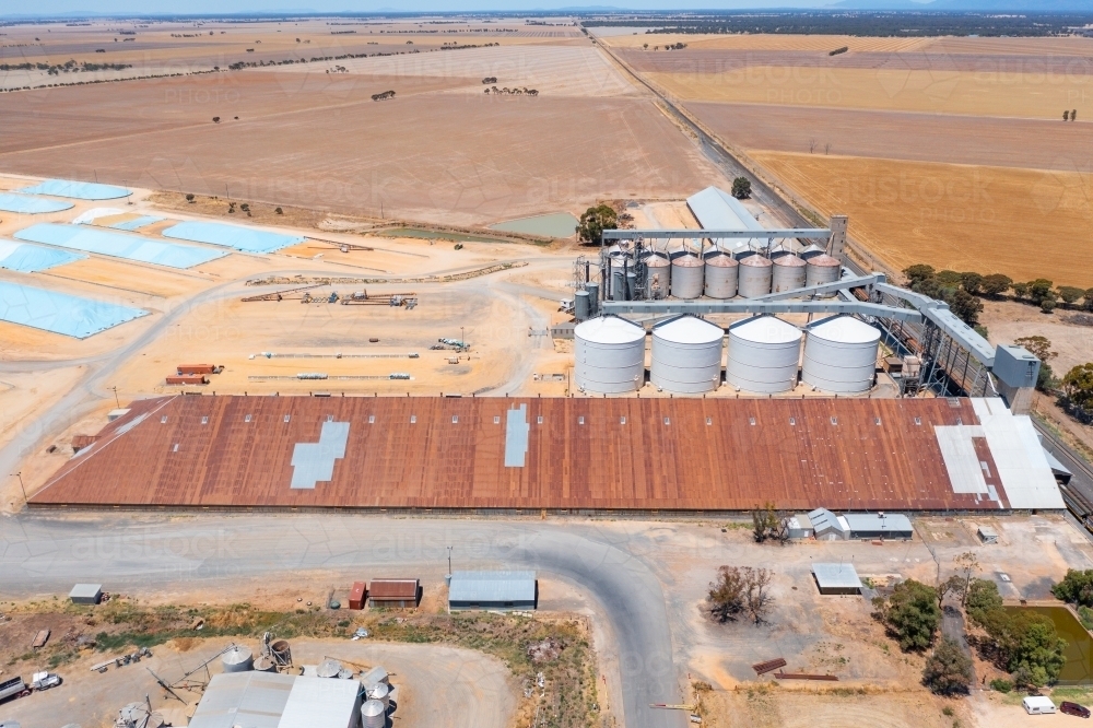 Aerial view of a long grain shed alongside silos and grain pits in a rural landscape - Australian Stock Image