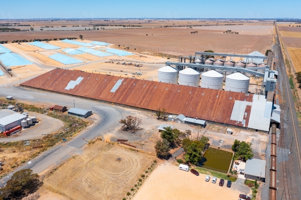 Aerial view of a long grain shed alongside silos and grain pits in a rural setting - Australian Stock Image