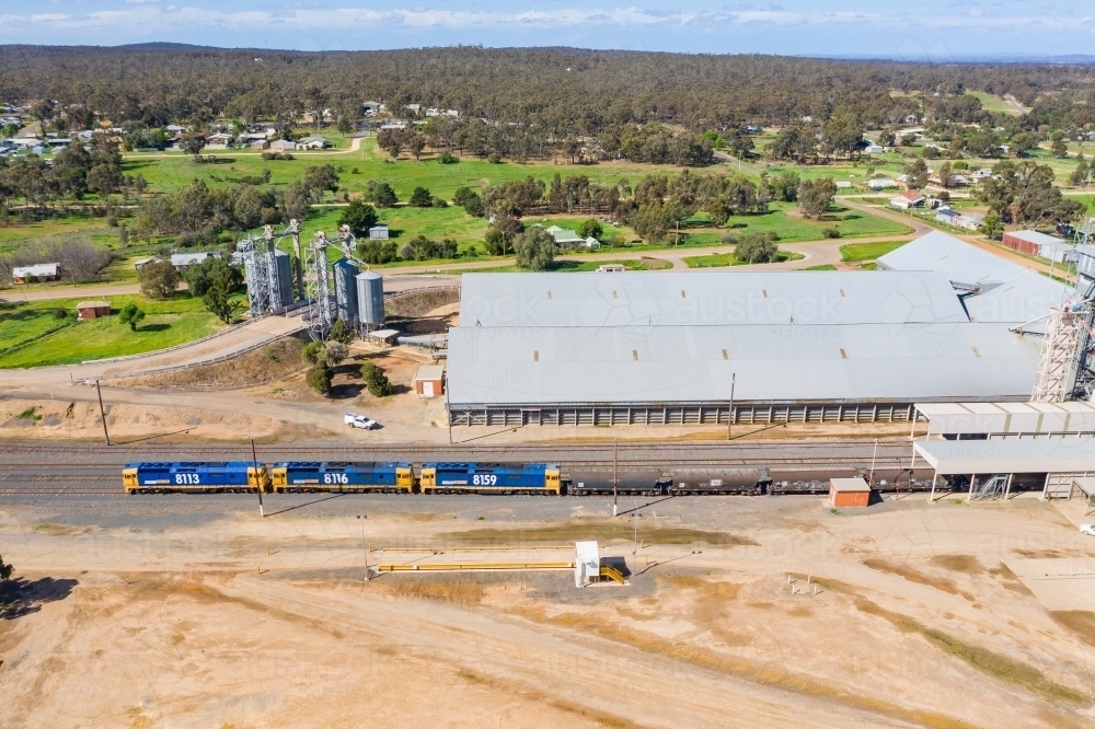 Aerial view of a long grain train waiting at a rural railway station - Australian Stock Image