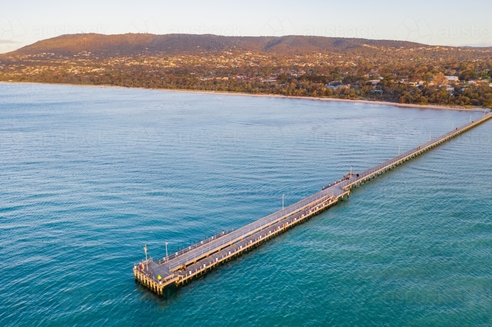 Aerial view of a long narrow jetty coming off a beach at sunset - Australian Stock Image