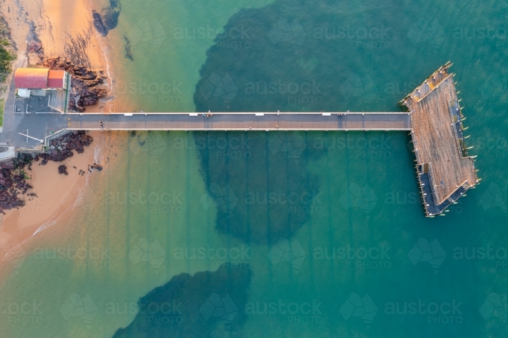 Aerial view of a long straight jetty leading out to a platform over a calm ocean bay - Australian Stock Image