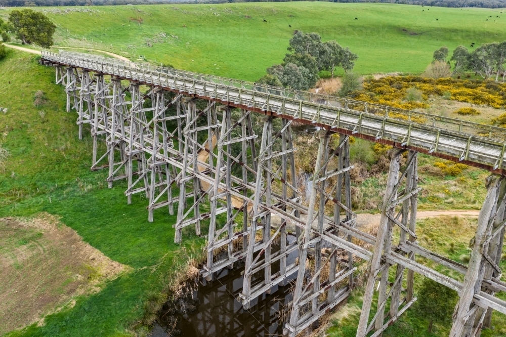 Aerial view of a long wooden trestle bridge across a green valley - Australian Stock Image