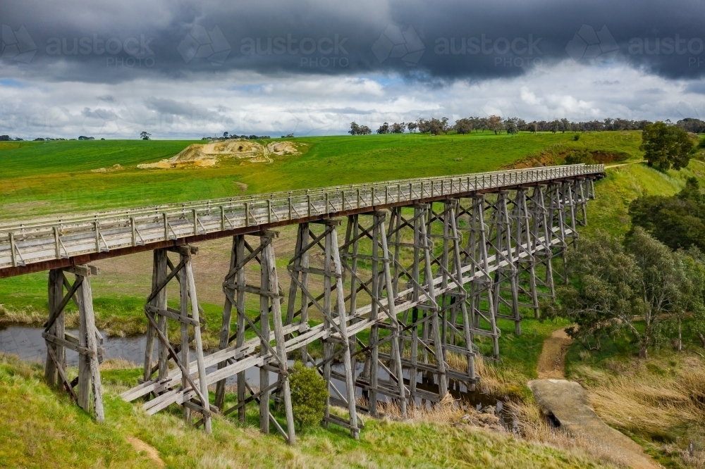 Aerial view of a long wooden trestle bridge across a green valley with dark clouds above - Australian Stock Image