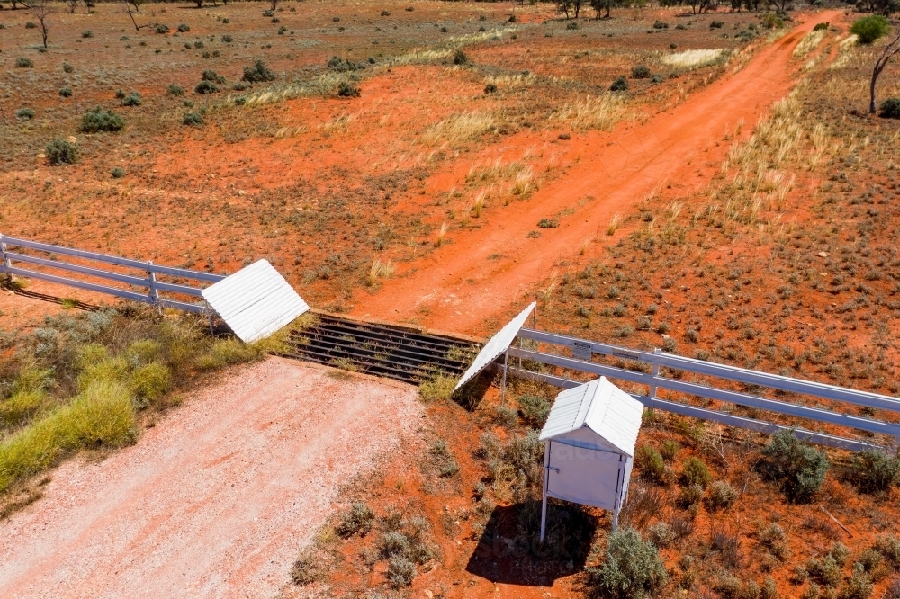 Aerial view of a mailbox and cattle grate in a dirt track across red barren land - Australian Stock Image