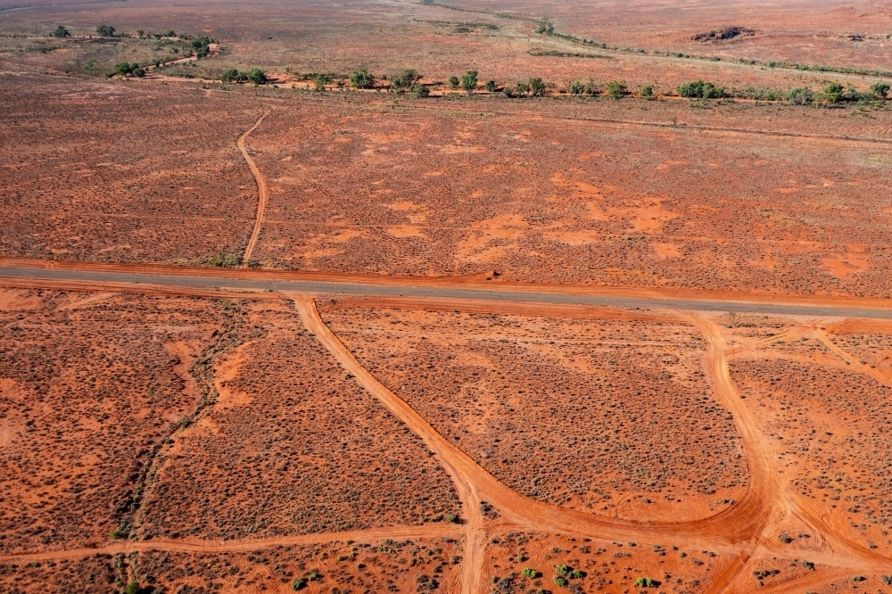 Aerial view of a narrow bitumen road and dirt tracks running through a dry red landscape - Australian Stock Image