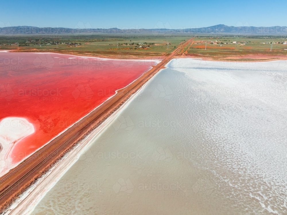 Aerial view of a railway line running across a salt lake with one side vivid red in colour - Australian Stock Image